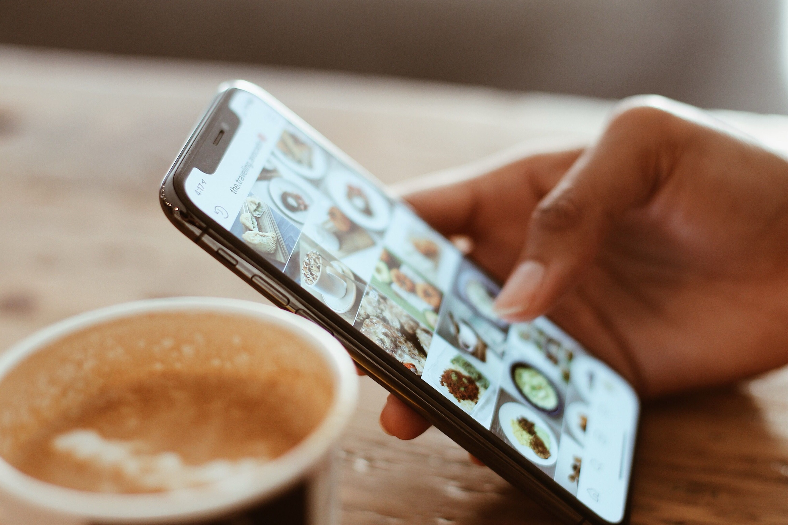 A hand scrolling Instagram on a phone next to a cup of coffee